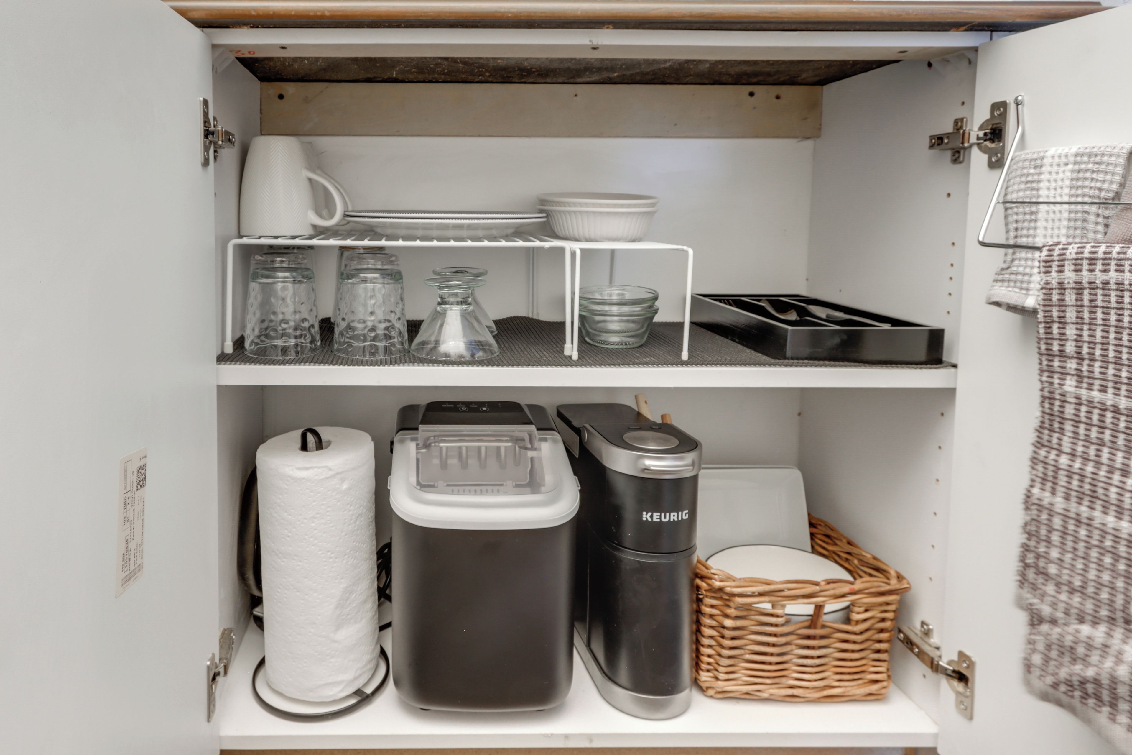 A kitchen cabinet with shelves holding various kitchen items, including a coffee maker, a basket, and glass containers.