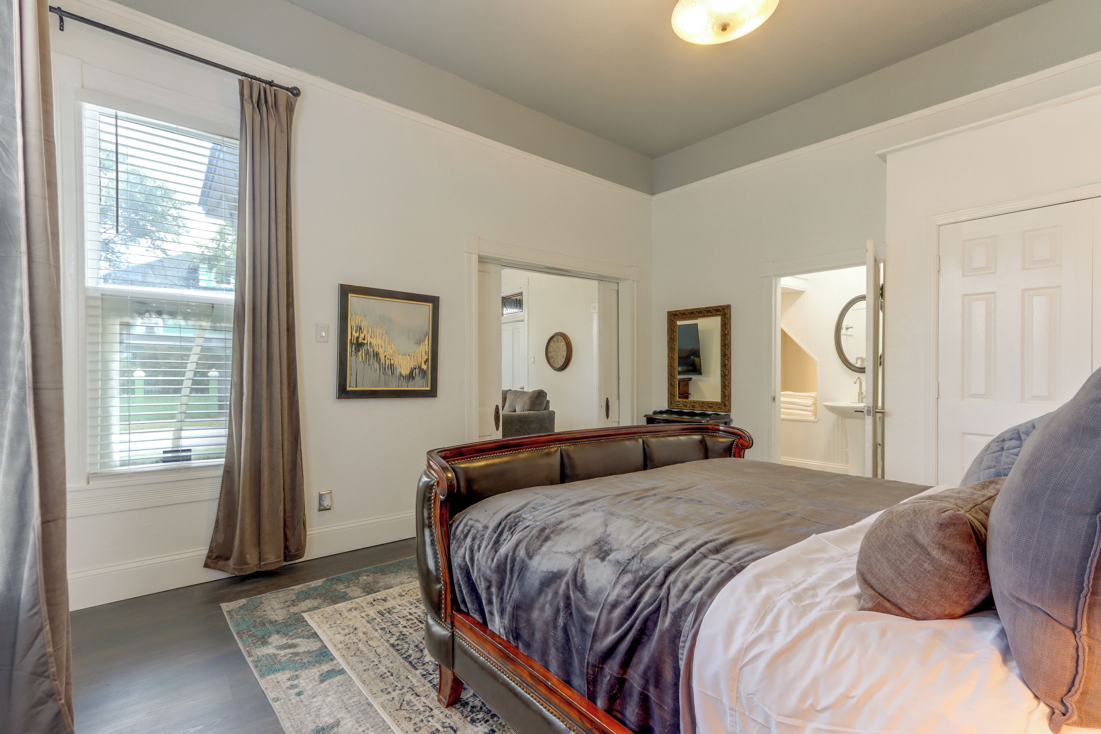 Une chambre avec un grand lit, une fenêtre avec des stores, une porte et un miroir.