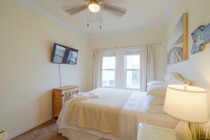A bedroom with a bed, a television mounted on the wall, a window with curtains, and a lamp on a bedside table. - Walk to Beach: Gulf Shores Gem, Pool & Water Views (Gulf Shores)