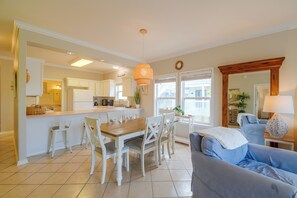 A modern kitchen with white cabinets, a dining area with a wooden table and white chairs, and a living room with a blue sofa. - Walk to Beach: Gulf Shores Gem, Pool & Water Views (Gulf Shores)