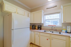 A kitchen with white cabinets, a refrigerator, a coffee maker, and a window with a view of buildings. - Walk to Beach: Gulf Shores Gem, Pool & Water Views (Gulf Shores)
