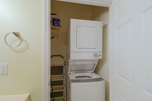 A laundry room with a stacked washer and dryer, a metal drying rack, and a shelf with cleaning supplies. - Walk to Beach: Gulf Shores Gem, Pool & Water Views (Gulf Shores)