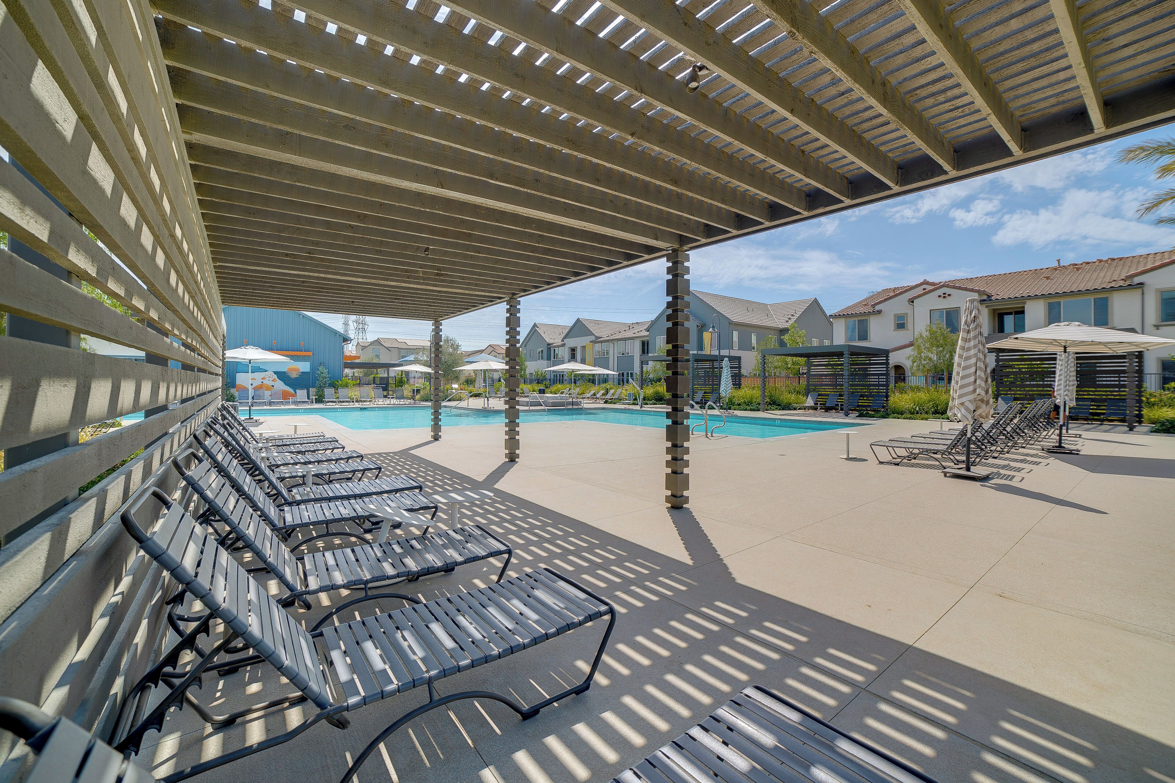 A covered outdoor area with lounge chairs and a swimming pool.