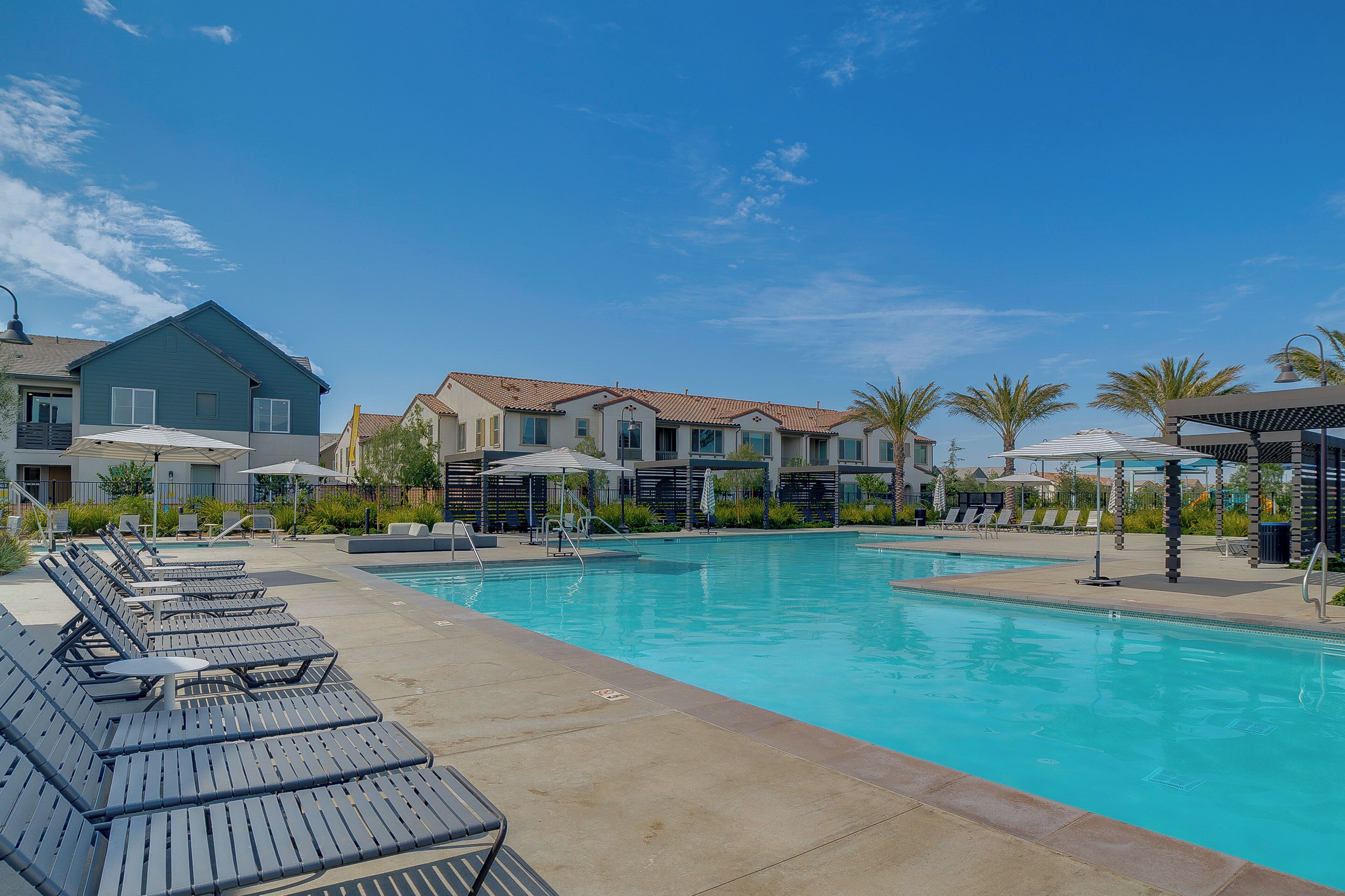 A swimming pool with lounge chairs and umbrellas, surrounded by buildings with a clear sky above.
