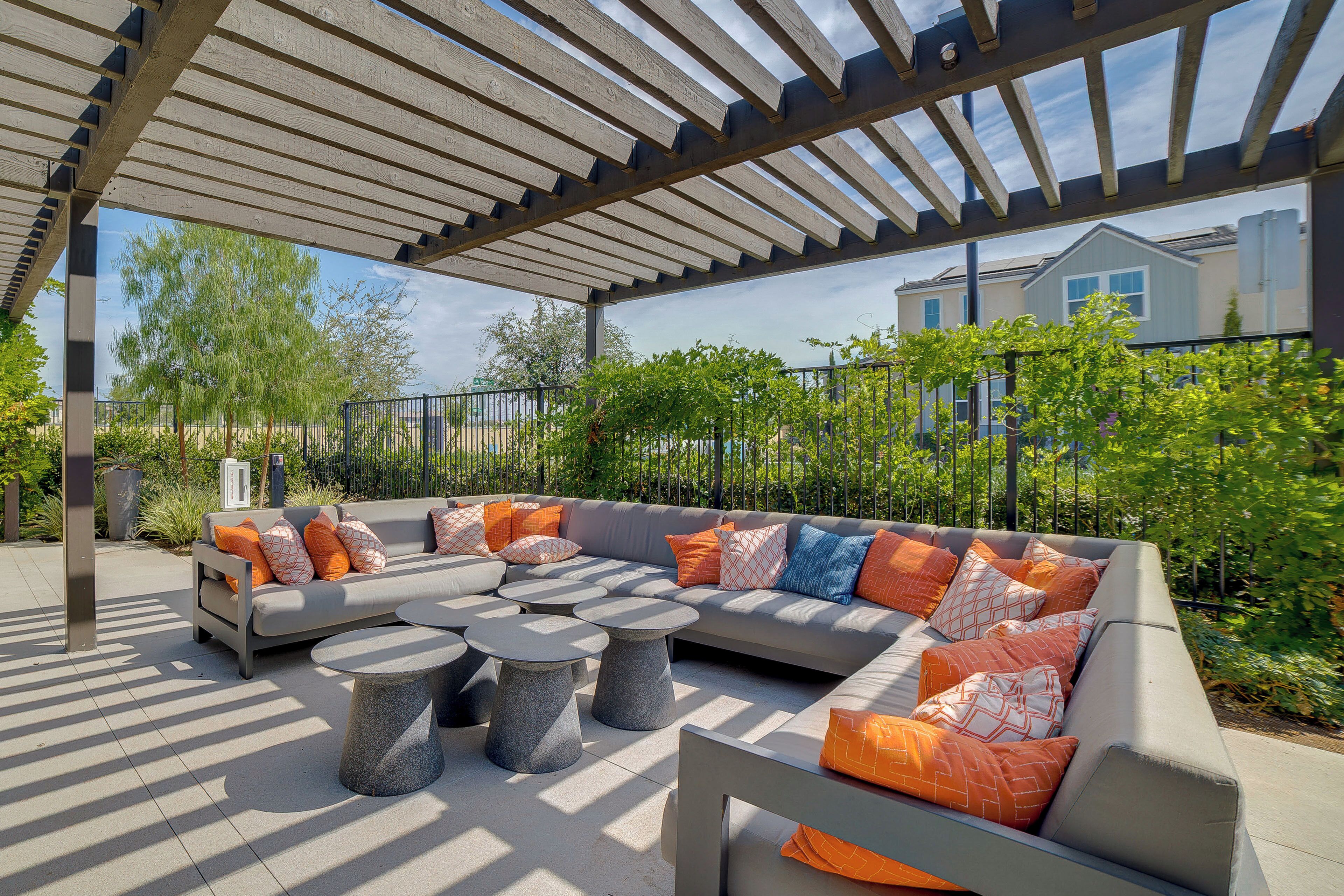 An outdoor seating area with a pergola, a sectional sofa, and round tables.