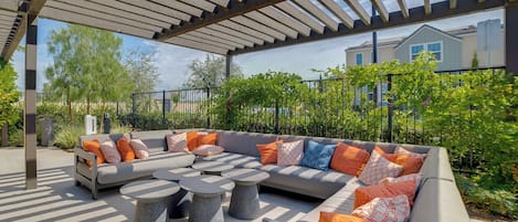 An outdoor seating area with a pergola, a sectional sofa, and round tables.