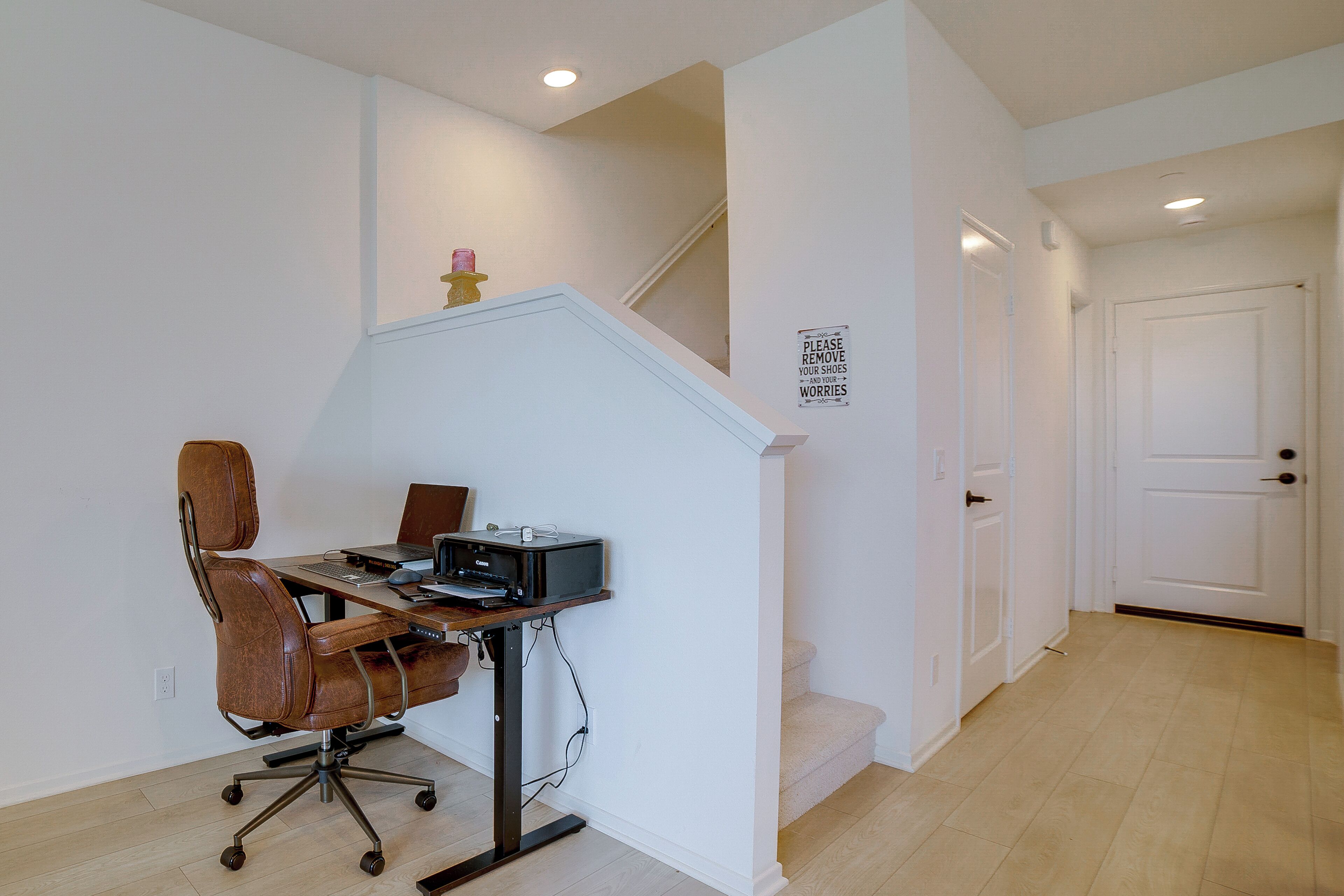A home office with a desk, chair, and printer. There is a staircase with a sign on the wall.
