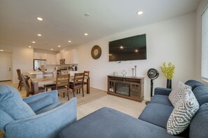 Een moderne woonkamer met een flatscreen televisie, een eethoek met houten meubels, en een keuken op de achtergrond.