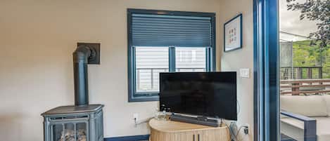 Ein Wohnzimmer mit Kaminofen, Flachbildfernseher und großem Fenster.