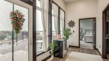 A hotel room with a balcony, a large window with curtains, a small table with a vase, and a bed with a headboard.