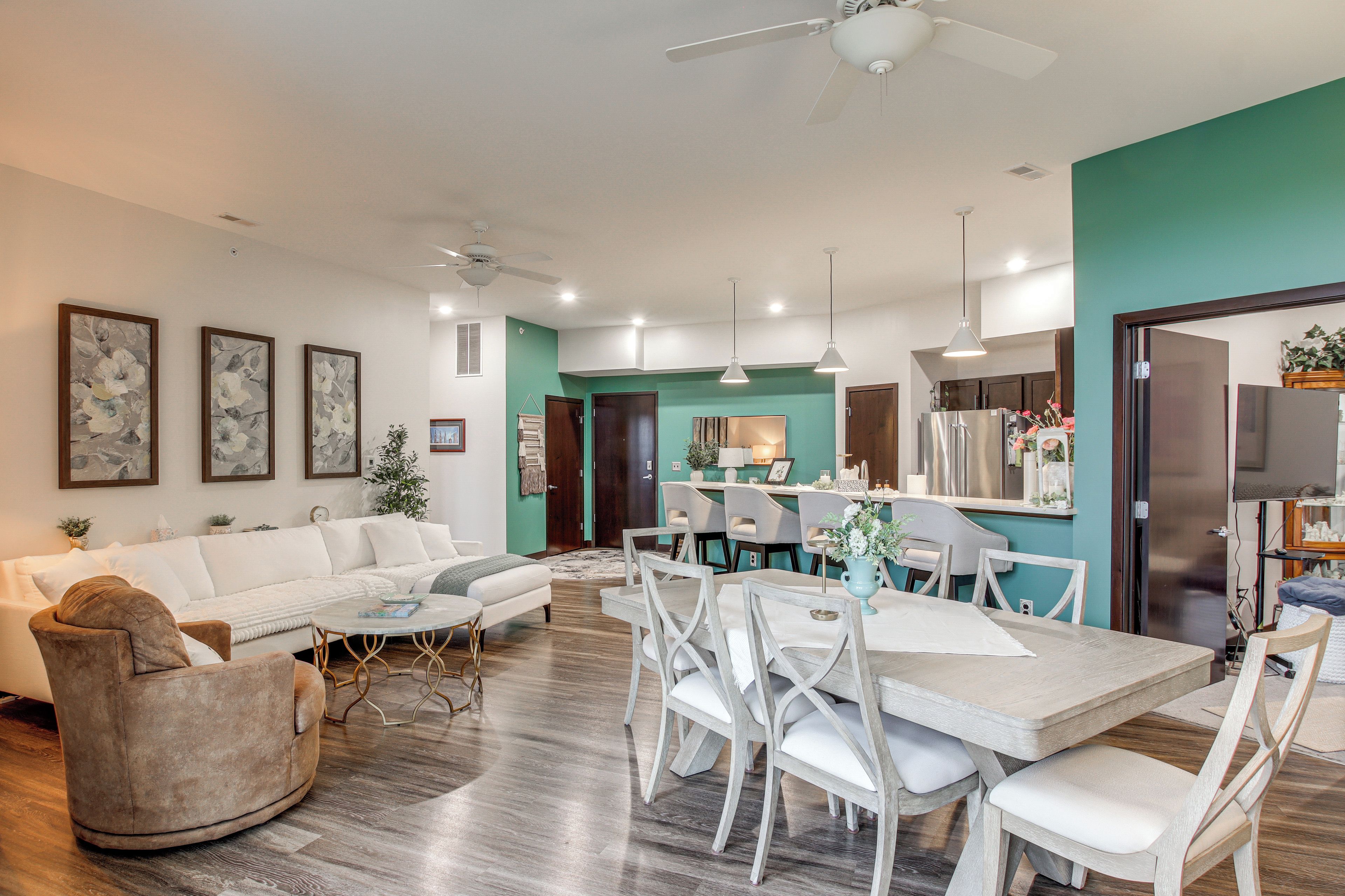 Un salon moderne avec un canapé blanc, une table à manger avec des chaises et un coin cuisine équipé d’un réfrigérateur et de placards.