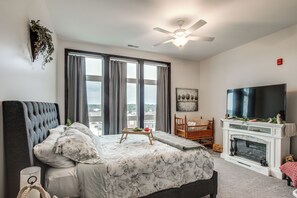 A bedroom with a bed, a television, a fireplace, and a large window.