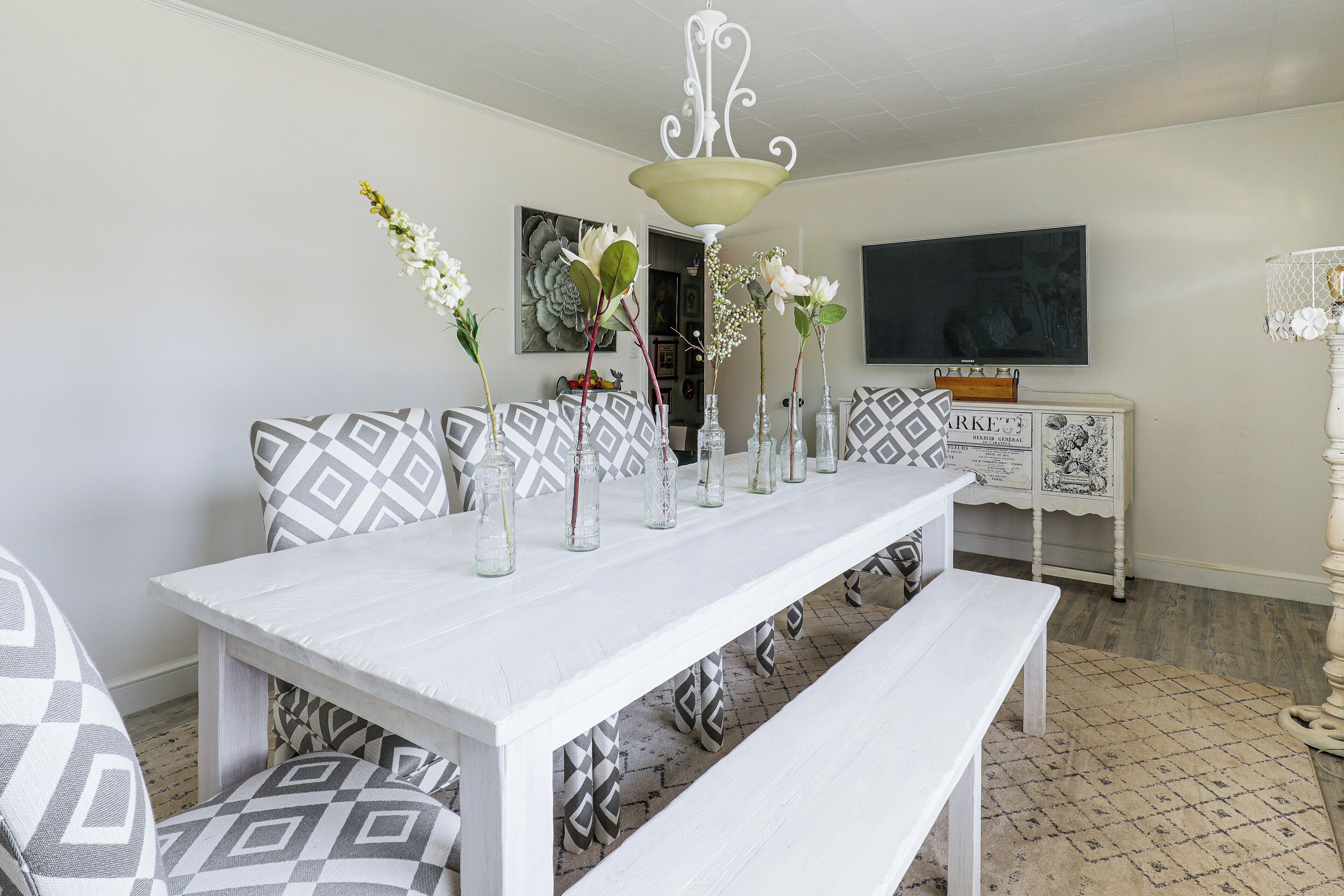Uma sala de jantar com mesa branca, almofadas estampadas e um banco.