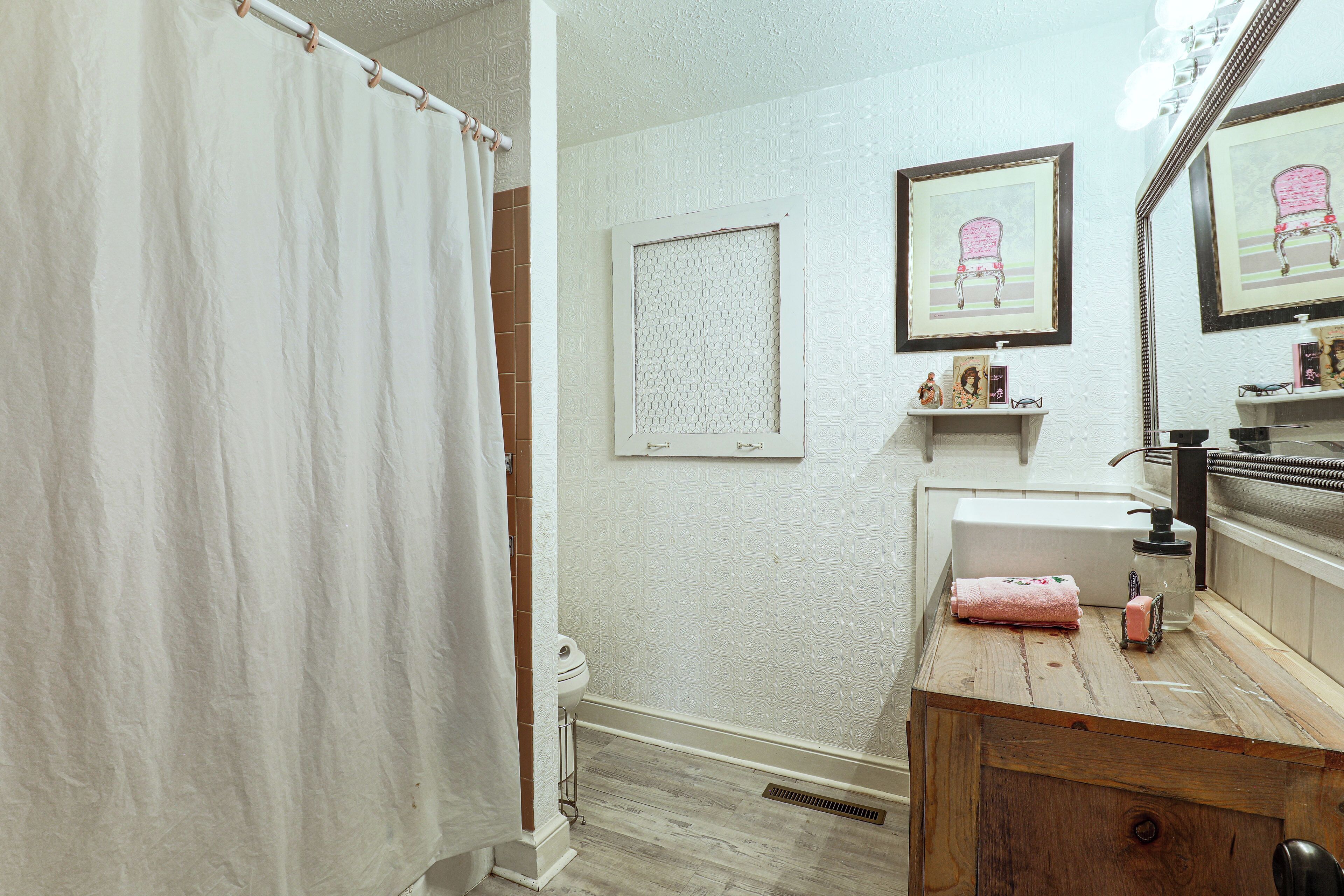 A bathroom with a shower curtain, a sink with a mirror, and a shelf with toiletries.