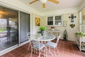 Eine überdachte Terrasse mit einem Glastisch und Stühlen, einem Deckenventilator und einem an der Wand befestigten Kruzifix.