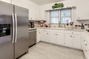 Eine Küche mit weißen Schränken, einem Edelstahl-Kühlschrank, einer Kaffeemaschine und einem Fenster mit Jalousien.
