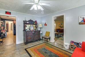 A living room with a ceiling fan, a wooden cabinet, a chair, a colorful rug, and a dining area in the background. - Wraparound Porch! Quiet Country Home, 9 Mi to MSU (Starkville)