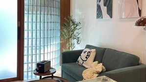 A modern living room with a glass partition, a sofa with a decorative pillow, and abstract wall art. - Nueng Rana 113 Unique House in Chinatown 3BR 2BA - Villa (Khet Samphanthawong)