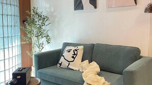 A modern living room with a green sofa, a small wooden table, and abstract wall art. - Nueng Rana 113 Unique House in Chinatown 3BR 2BA - Villa (Khet Samphanthawong)