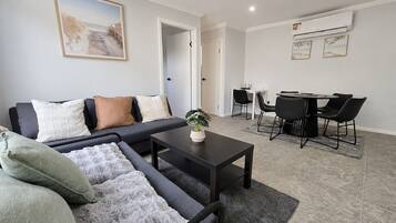 A modern living room with a sofa, a coffee table, and a dining area with chairs and a table.