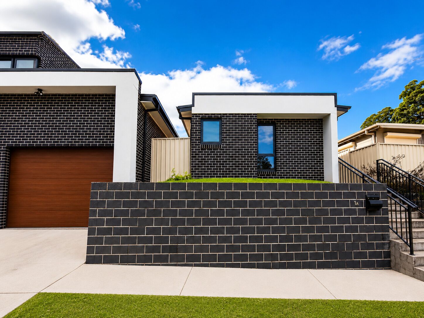 A modern residential building with a garage, a brick facade, and a small front yard.