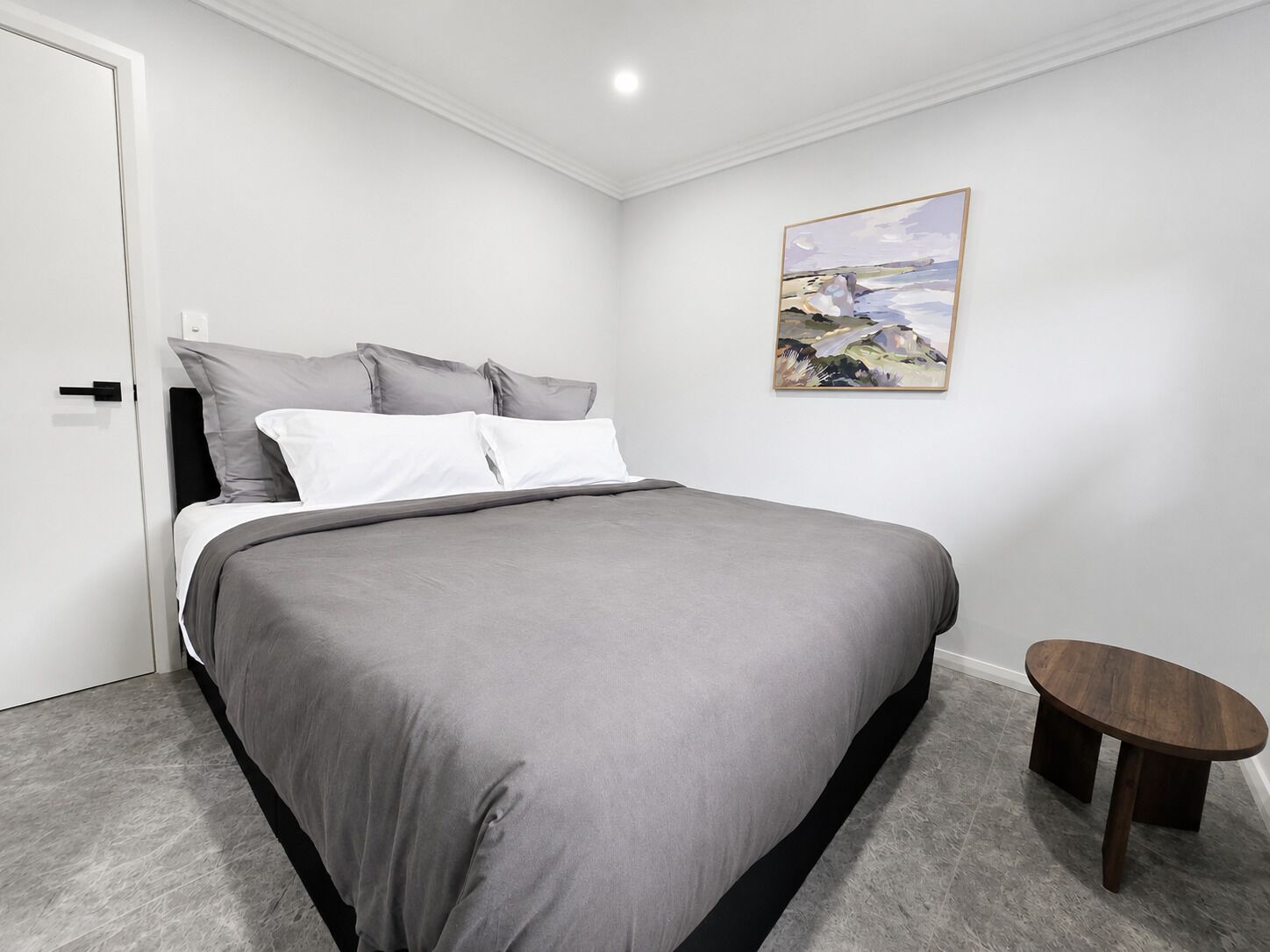 A bedroom with a bed, a small table, and a painting on the wall.