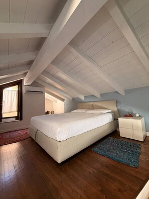 Ein Schlafzimmer mit schrägem Dach, einem Bett, einem Nachttisch und einem Fenster.