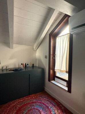 A room with a sloped ceiling, a window with a curtain, a dark-colored dresser, and a colorful rug. - Marvelous 1-bedroom apartment with AC in vibrant Cagliari (Cagliari)