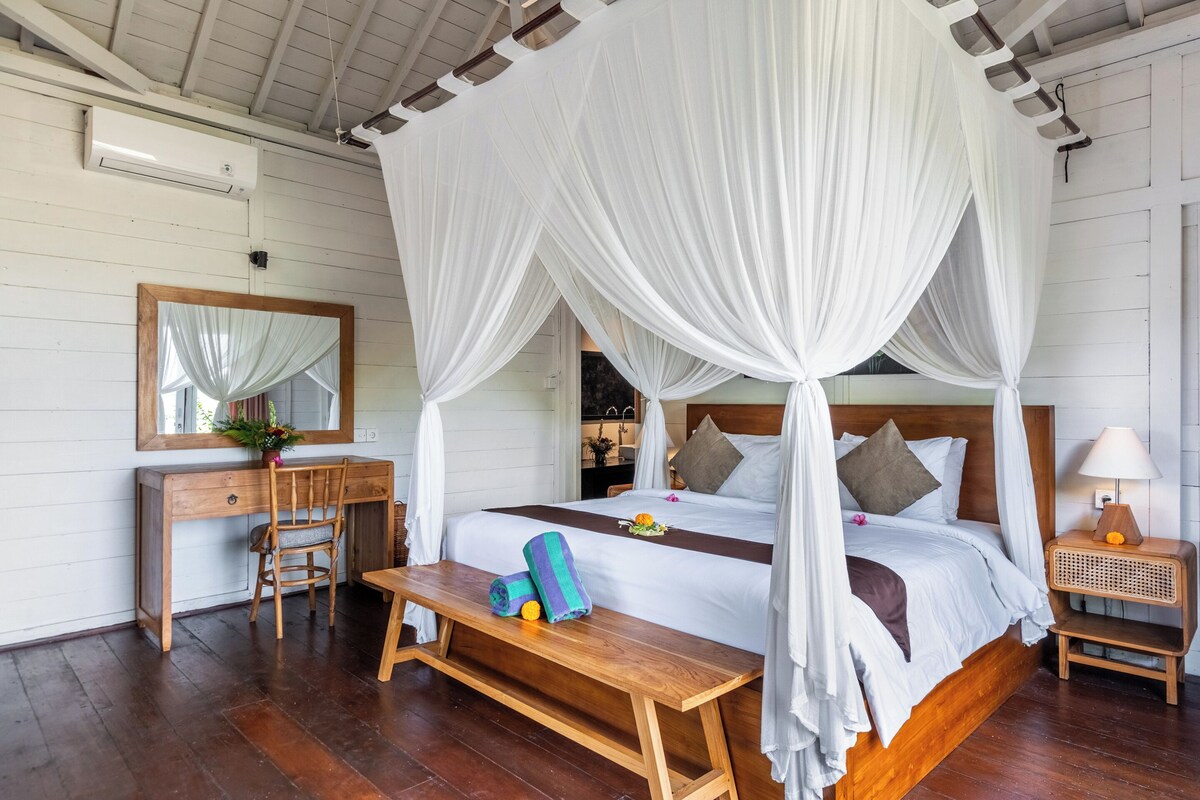 A room with a four-poster bed, a wooden desk, a chair, a bedside table, and a bench.