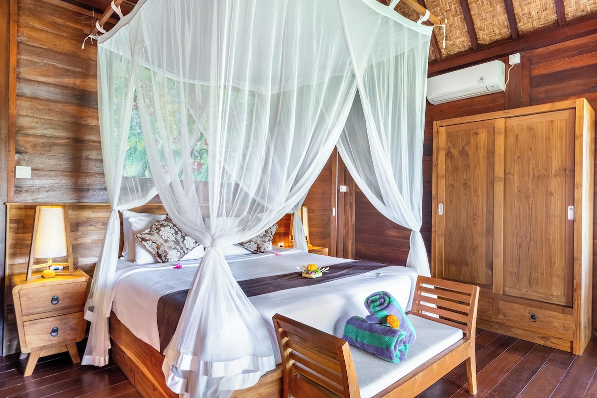 A wooden room with a bed under a canopy, a nightstand with a lamp, a wooden chair, and a wardrobe.