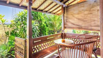 Una terraza de madera con una mesa y sillas, rodeada de abundante vegetación y vistas al paisaje.