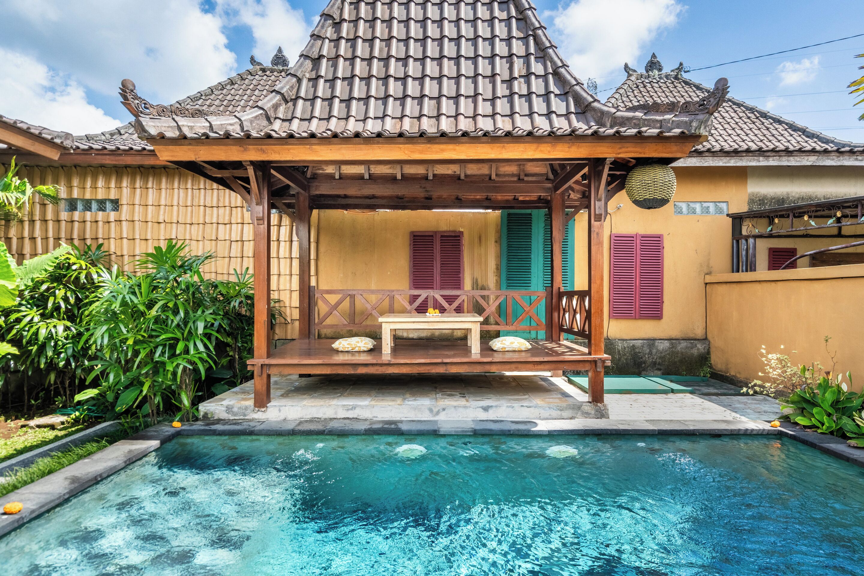 A traditional wooden gazebo with a tiled roof, a small pool, and a garden with tropical plants.
