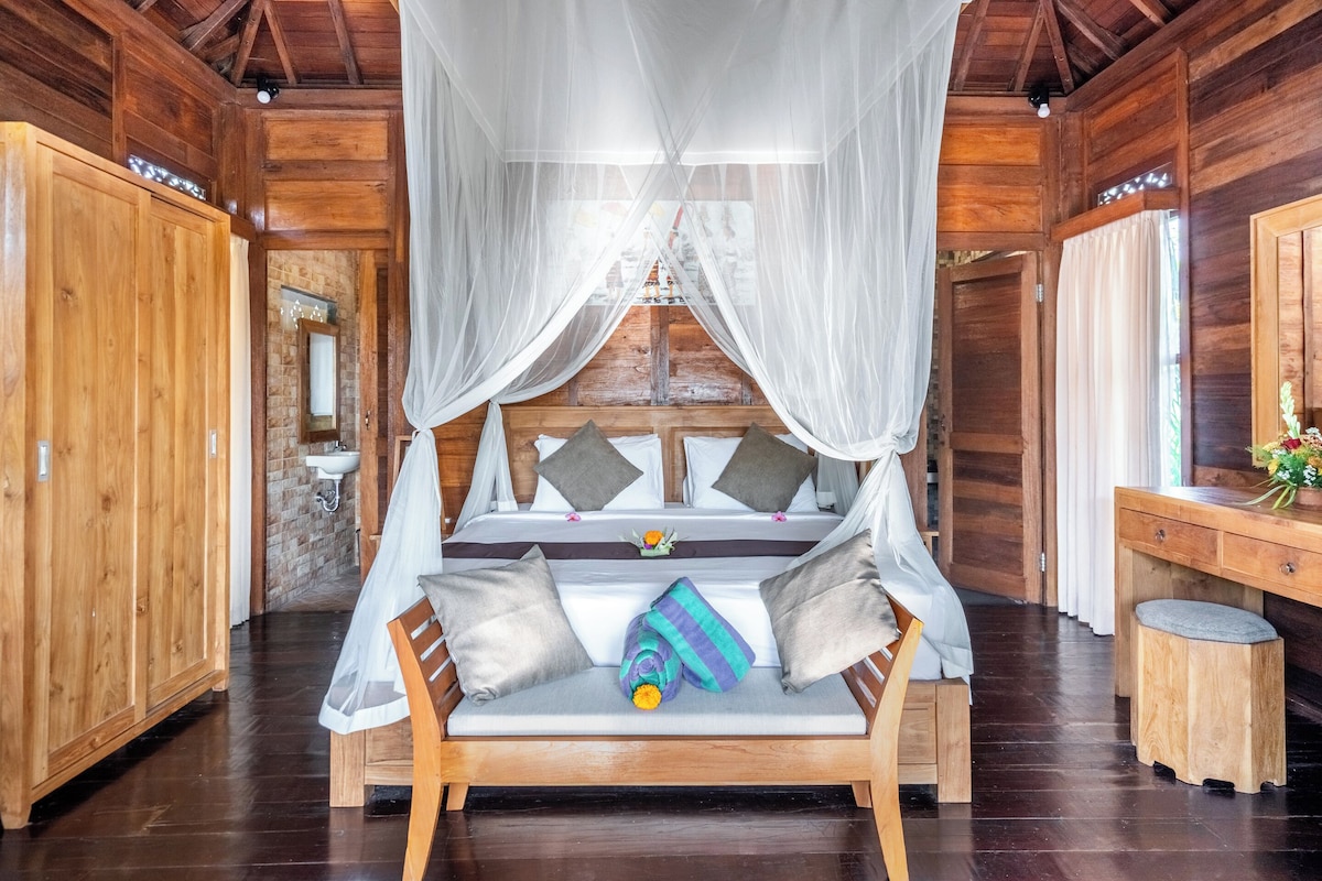 A wooden room with a bed under a canopy, a wooden desk, and a mirror.