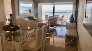 Un saló modern amb una taula de dinar de vidre, sofàs beix i vista a la platja.