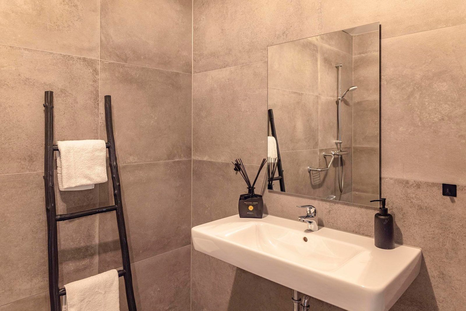 Een badkamer met een witte wastafel, een spiegel, een handdoekhouder en een douche.