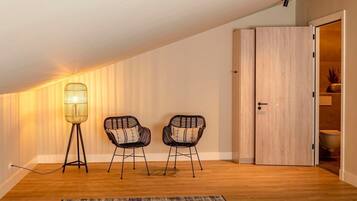 Een kamer met een schuine kap, twee stoelen met kussens, een vloerlamp en een houten deur.