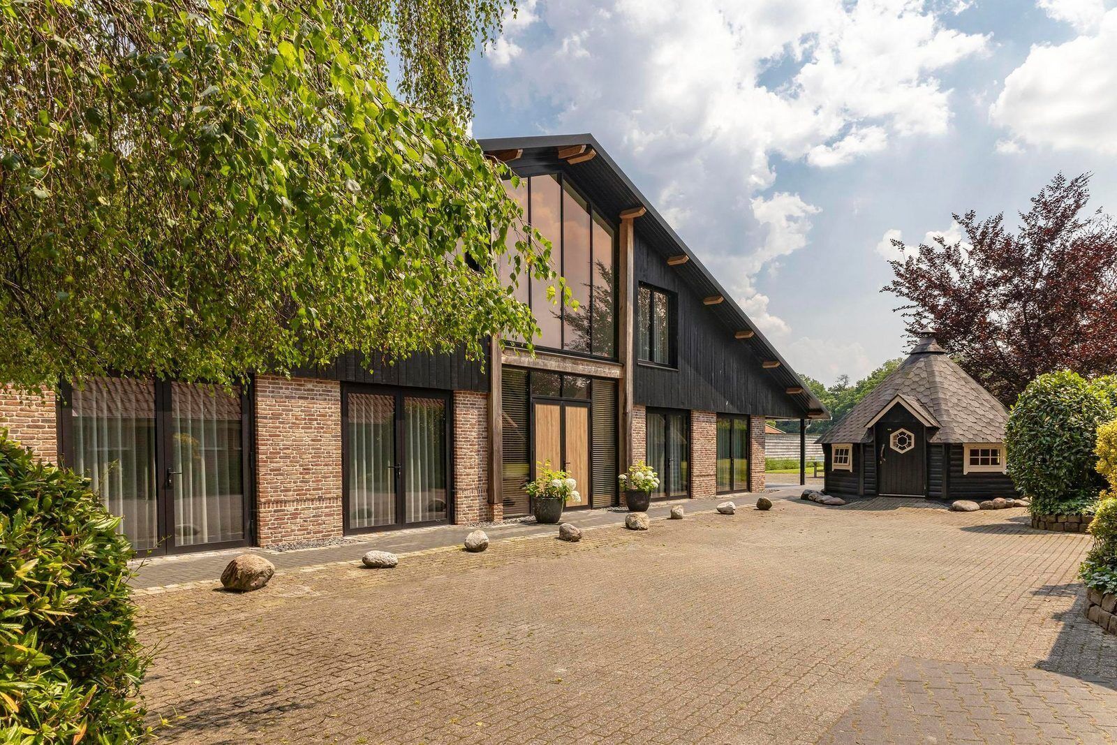 Een modern gebouw met een bakstenen gevel, grote ramen en een klein aangrenzend gebouwtje met een kegelvormig dak.