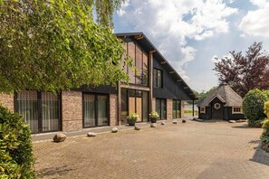 Een modern gebouw met een bakstenen gevel, grote ramen en een klein aangrenzend gebouwtje met een kegelvormig dak.