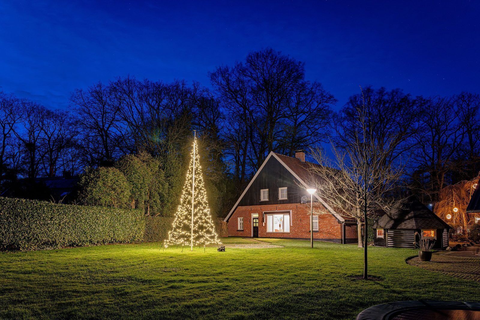 Een huis met een goed verlichte voortuin, een kerstboom en een kleine schuur.