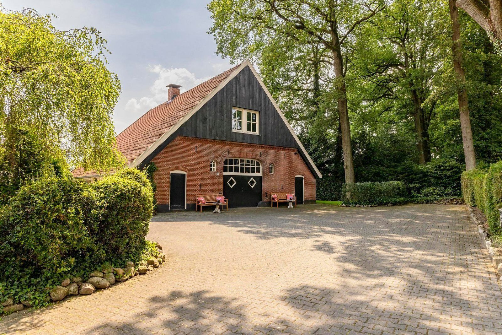 A traditional wooden house with a sloped roof, a brick facade, and a paved driveway.