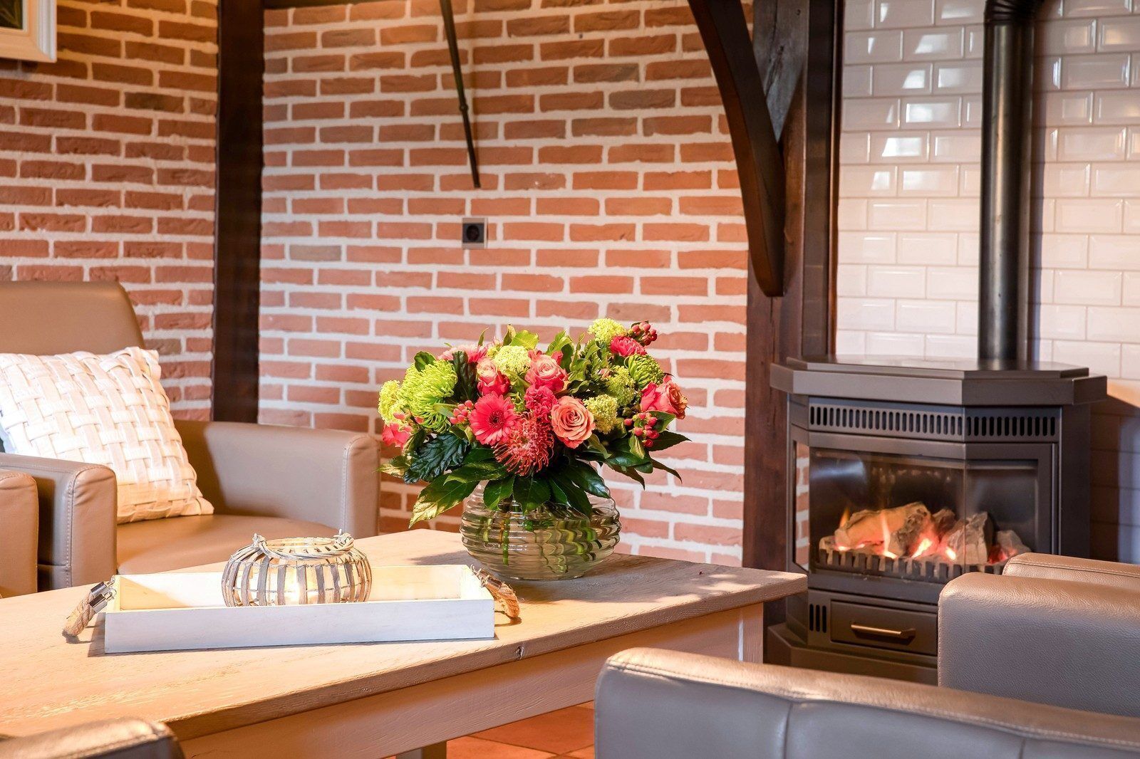 Un salon chaleureux avec un mur en briques, une cheminée et une table ornée d’un vase de fleurs.