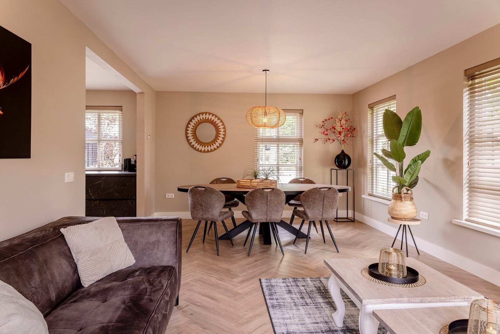 Een moderne woonkamer met een donkerbruine bank, een eettafel met stoelen, een salontafel en een groot raam met zonwering.