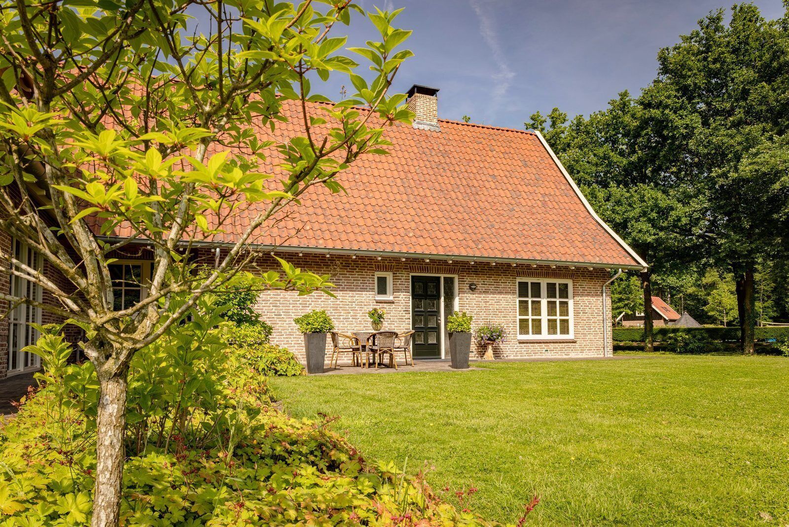 Une maison en briques avec un toit en tuiles, une porte d’entrée et un petit porche avec des chaises.