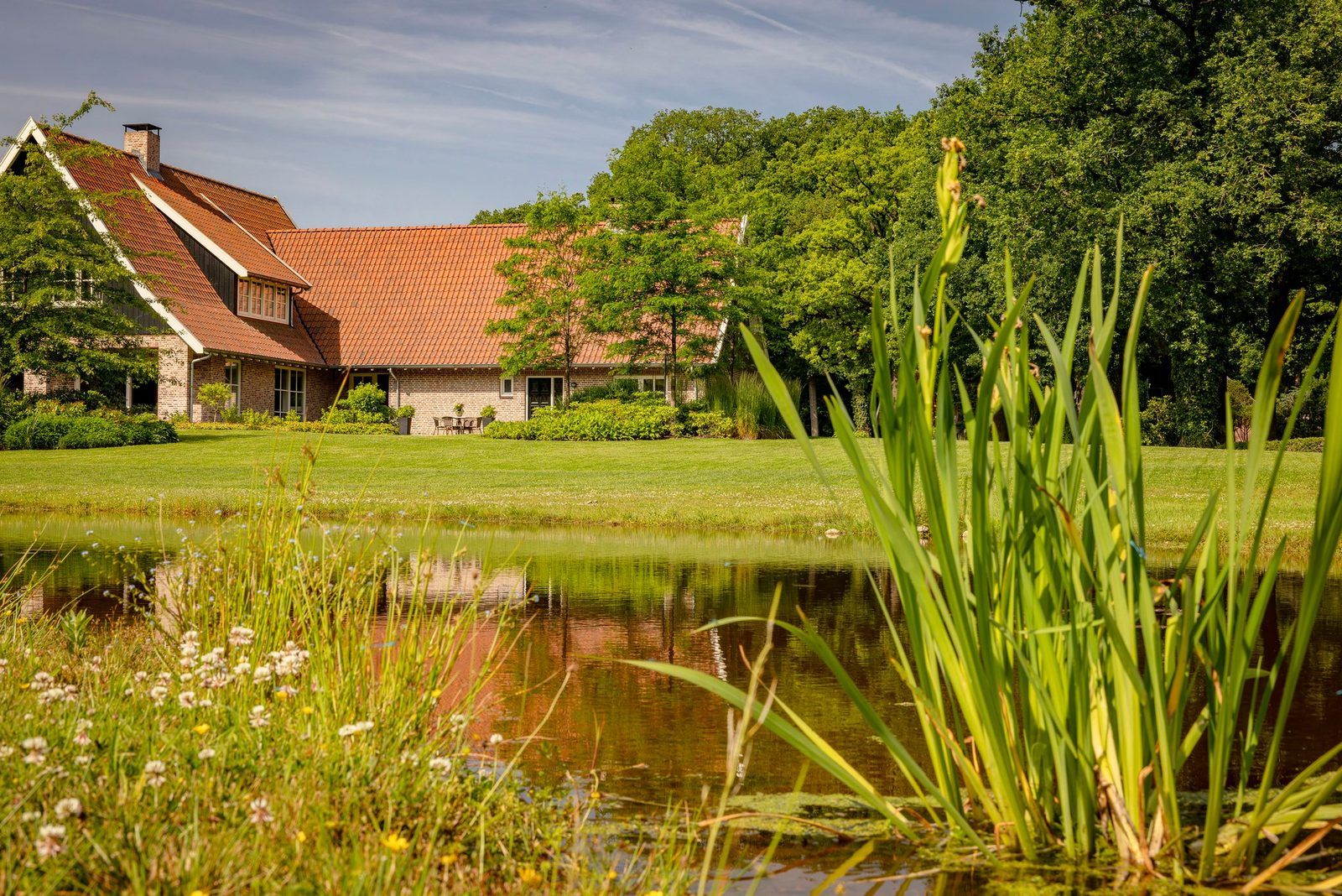 Ein Haus mit geneigtem Dach, einem Teich im Vordergrund und einem gepflegten Rasen.