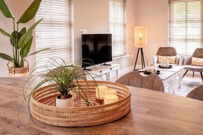 Een moderne woonkamer met een houten salontafel, een gevlochten mand met een plant, een televisie en een vloerlamp.