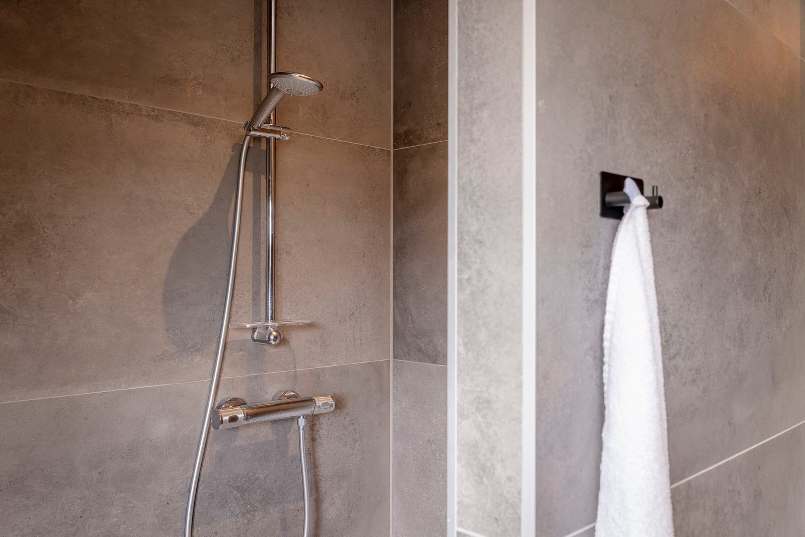 Eine Dusche mit Duschkopf zum Abnehmen und einem fest montierten Handtuchhalter.