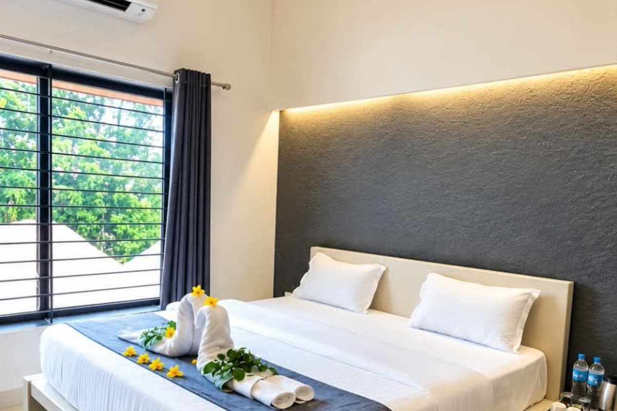 Una habitación de hotel moderna con una cama grande, una mesita de noche y un ventanal con cortinas.