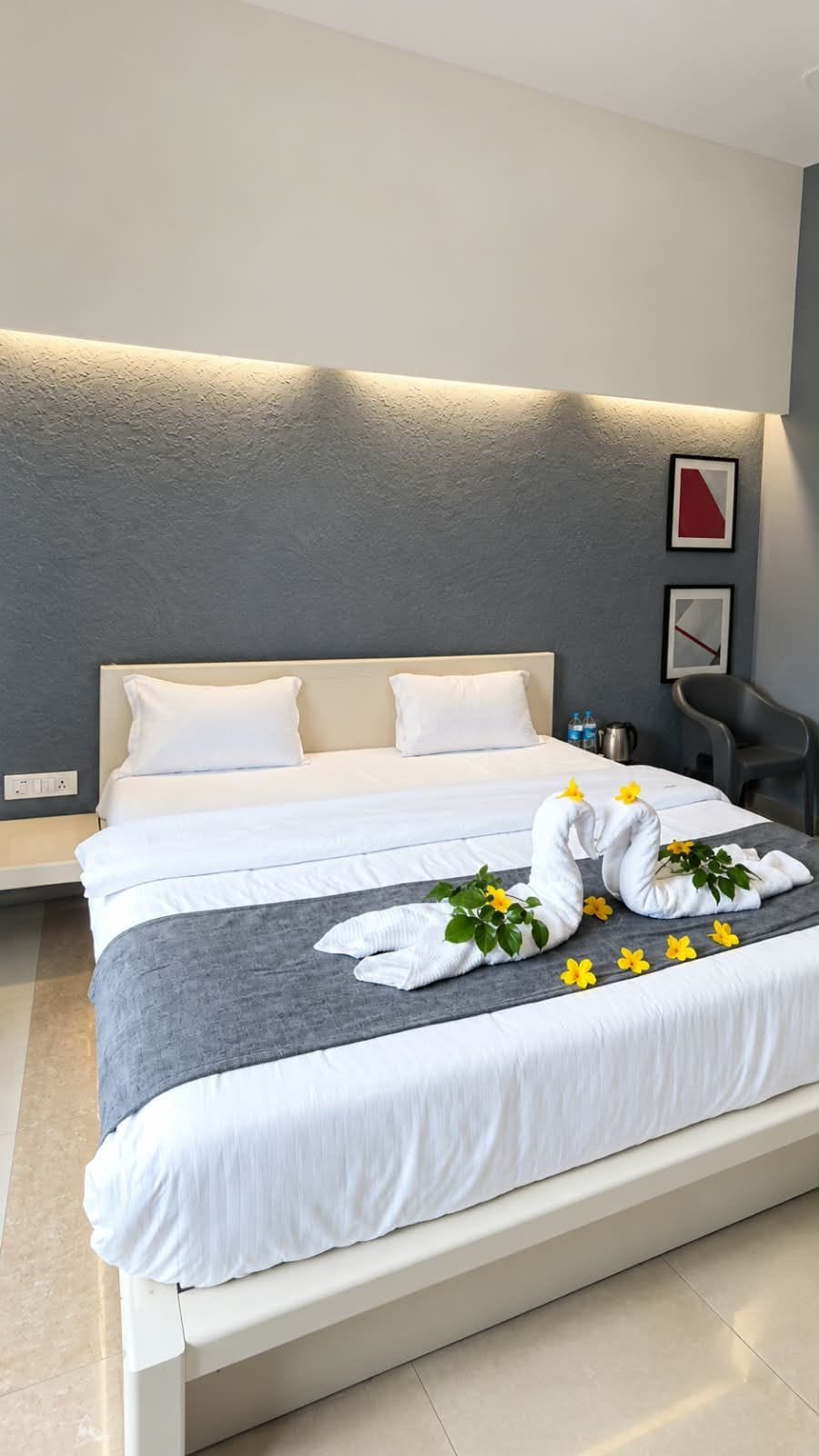 A modern hotel room with a large bed, a bedside table with a lamp, and a wall-mounted artwork.