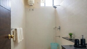 Casa de banho compacta com sanita, lavatório, suporte de toalhas, chuveiro e uma pequena planta em vaso.