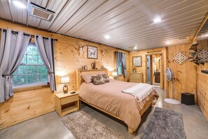 Quarto de cabana de madeira com cama, mesas de cabeceira, luminária e ventilador.